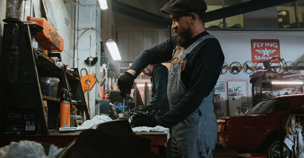 Mécanicien effectuant des réparations dans un garage vintage, utilisant des outils et des machines.