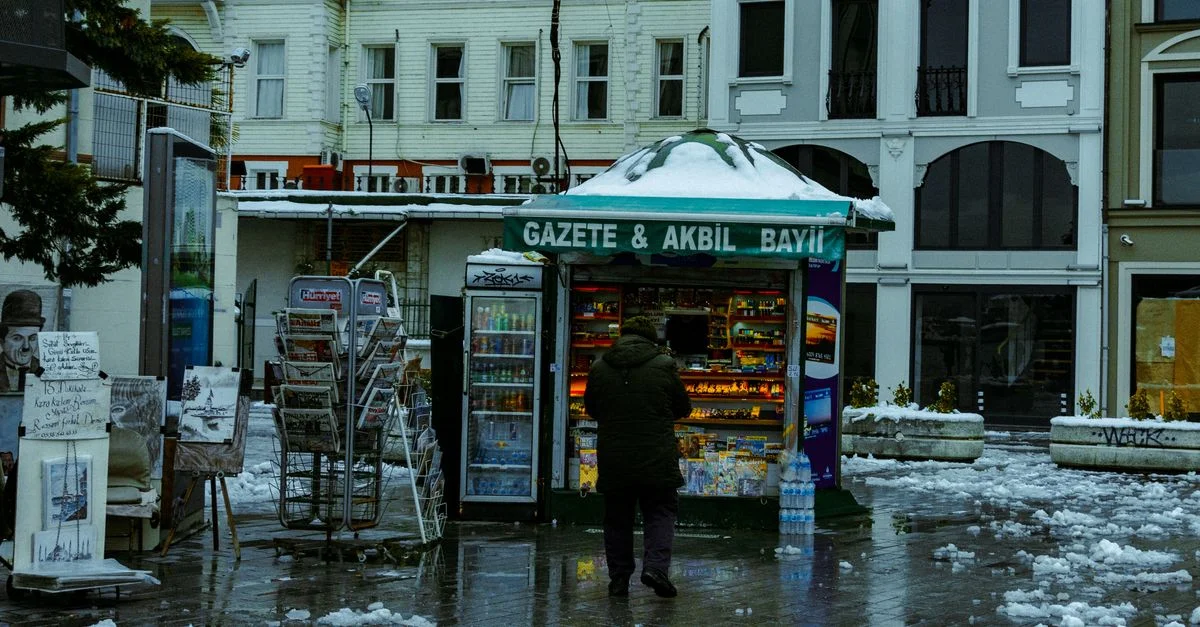 Un homme s'approche d'un kiosque à journaux couvert de neige par un jour d'hiver humide dans la ville.