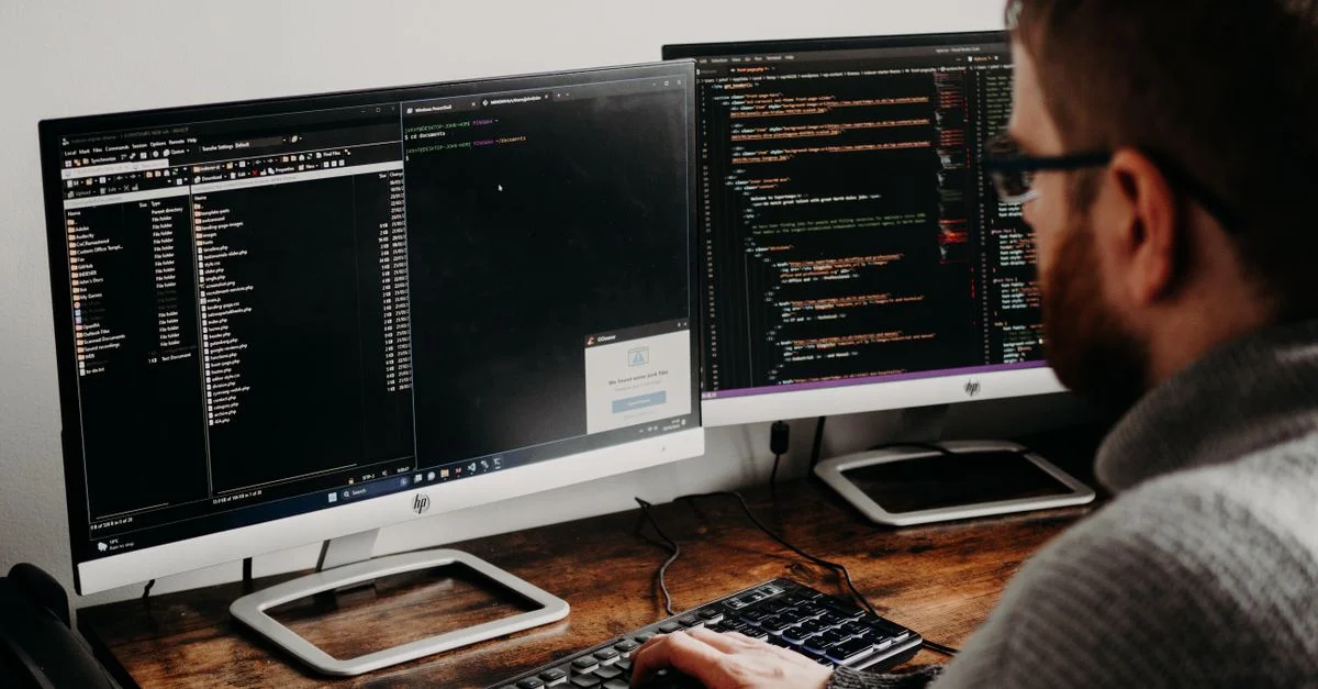 Développeur de logiciels tapant du code sur des écrans doubles à un bureau en bois.