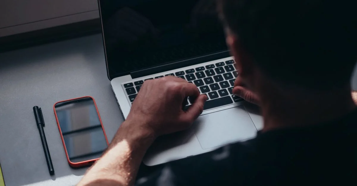Gros plan d'un homme travaillant sur un ordinateur portable avec un smartphone et un stylo sur la table.