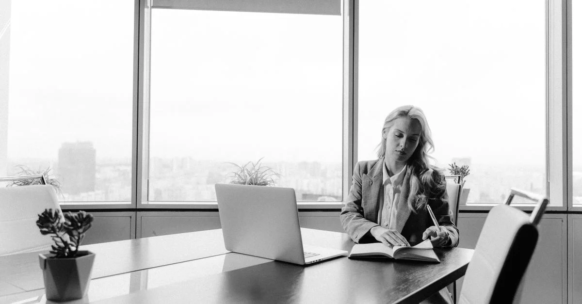 Femme d'affaires travaillant à un bureau dans un bureau lumineux avec vue sur la ville, en noir et blanc.