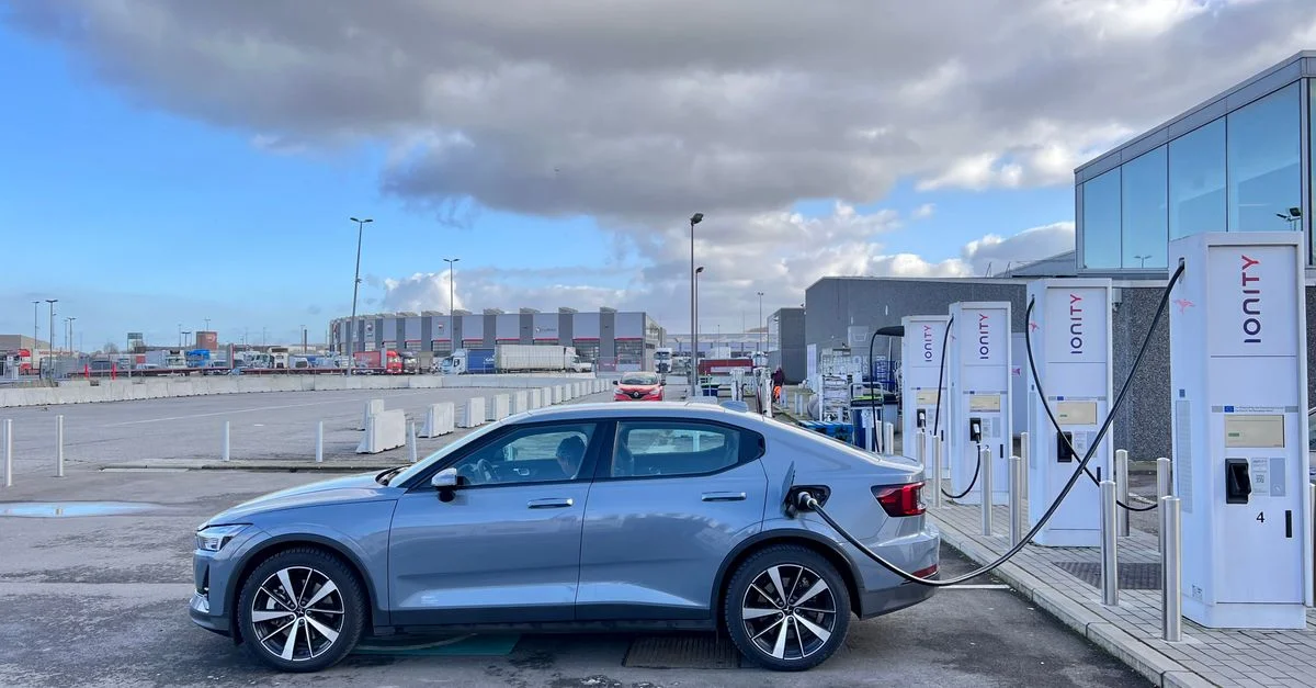 Une voiture électrique élégante en charge à une station Ionity par une journée nuageuse dans une zone industrielle.