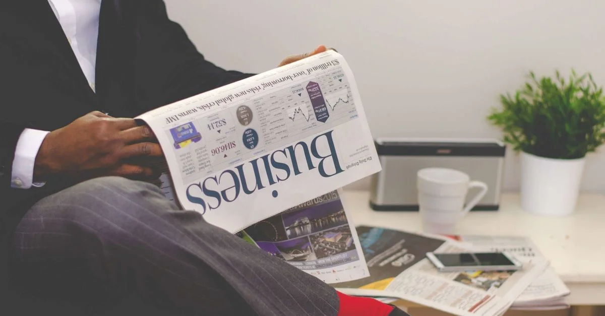 Homme d'affaires lisant un journal financier à un bureau, soulignant le thème de la finance et du commerce.