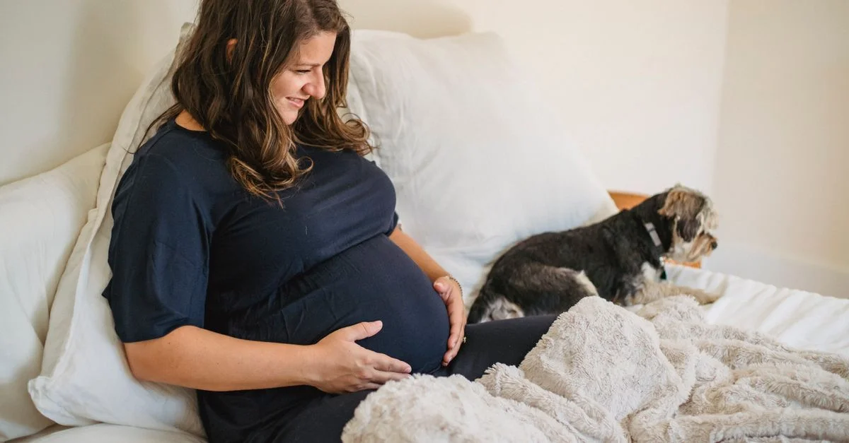Une femme enceinte se détendant sur le lit avec son chien, profitant d'un moment chaleureux à l'intérieur.