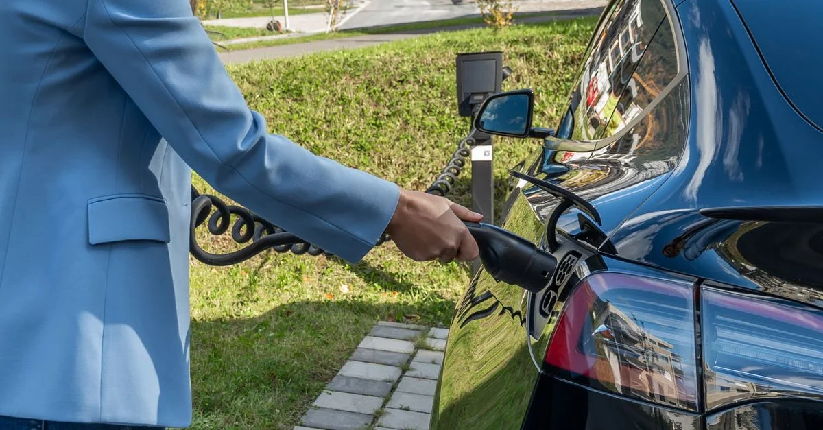 Une personne branche une voiture électrique à une borne de recharge extérieure, illustrant la transition énergétique verte.